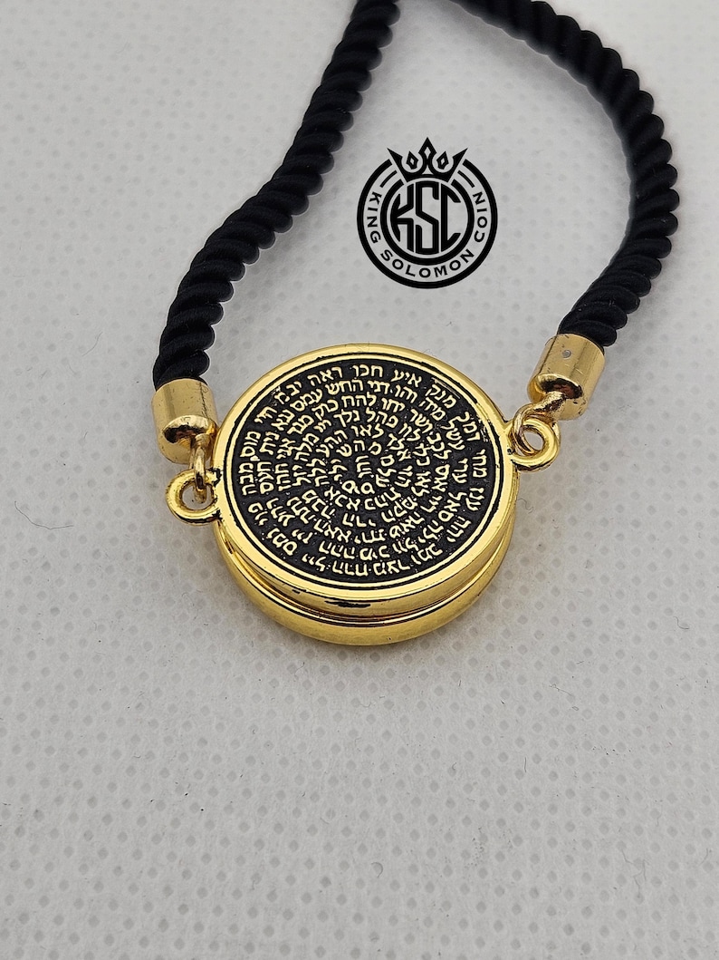 May include: A gold-colored pendant with black text and a black rope necklace. The pendant has a circular design with Hebrew text and the words "King Solomon Coin" in a logo. The necklace is displayed against a light background.