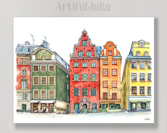 May include: Watercolor painting of a row of colorful buildings in a European city. The buildings are painted in shades of red, orange, yellow, and green. The painting is signed "Julia" in the bottom right corner.