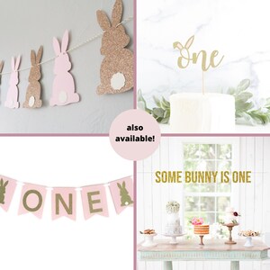 May include: Pink and gold glitter bunny banner with the word "ONE" in gold glitter. Also included is a gold glitter cake topper with the word "ONE" and a banner that says "SOME BUNNY IS ONE".