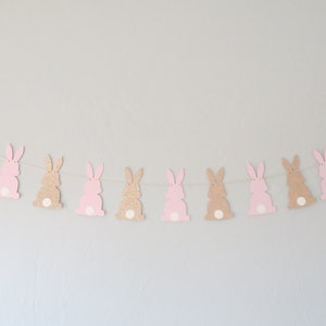 May include: A garland of pink and brown glitter bunny cutouts strung on a white string. The bunnies have white spots on their tails.