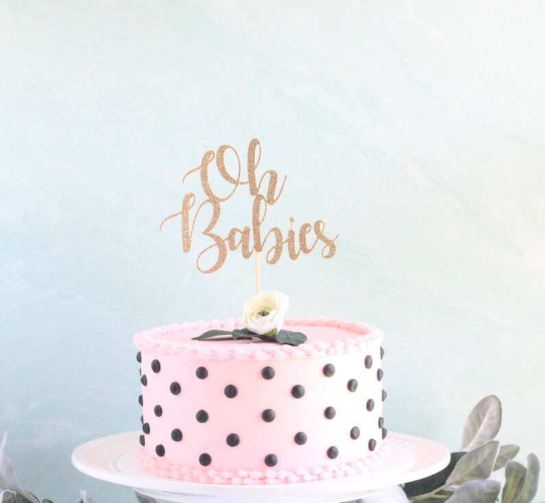 Op de afbeelding: Roze cake met zwarte stippen en een gouden glitter caketopper met de tekst "Oh Babies".