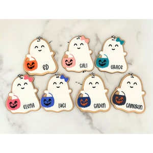 May include: Seven wooden ghost ornaments with different coloured candy buckets and names written on them: Ed, Cali, Grace, Elena, Luci, Caden, and Cameron.