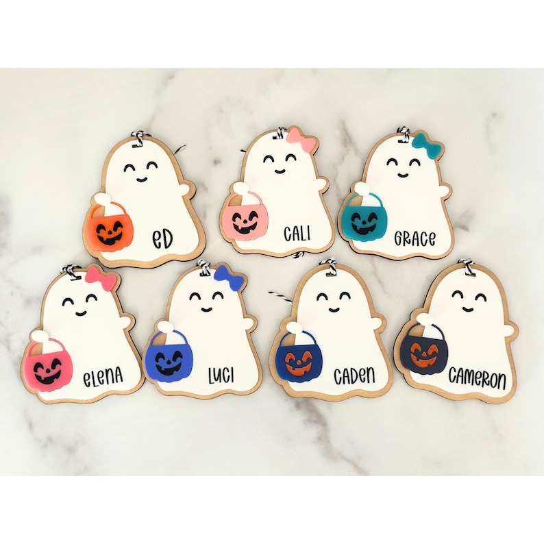 May include: Seven wooden ghost ornaments with different coloured candy buckets and names written on them: Ed, Cali, Grace, Elena, Luci, Caden, and Cameron.