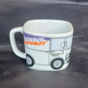 May include: White ceramic mug with a square shape and a handle. The mug features a cartoon illustration of a white Federal Express delivery truck with the words "Federal Express" and "Worldwide Service" printed on the side.
