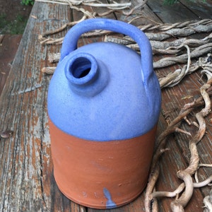 May include: A blue and brown ceramic pitcher with a handle. The pitcher has a wide mouth and a rounded body. It is sitting on a wooden surface.