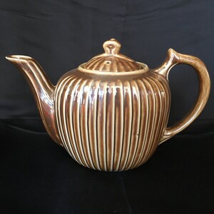May include: A brown ceramic teapot with a ribbed design and a lid. The teapot has a spout and a handle.