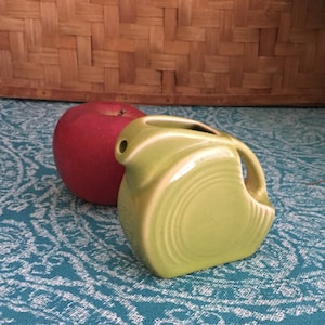 May include: A green ceramic pitcher with a rounded body and a spout. The pitcher has a white rim and a white stripe around the middle.