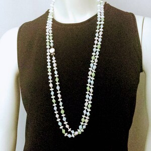 May include: A long, layered necklace with white, green, and pale blue beads. The necklace is displayed on a mannequin wearing a black sleeveless top. The beads are strung together with small white beads.