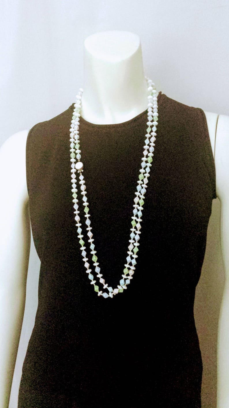 May include: A long, layered necklace with white, green, and pale blue beads. The necklace is displayed on a mannequin wearing a black sleeveless top. The beads are strung together with small white beads.