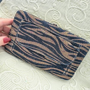 May include: A rectangular wallet with a zebra stripe pattern in navy blue and gold. The wallet has white stitching around the edges and a small pocket on the front. The wallet is made of a textured fabric.