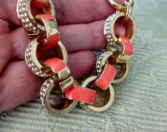 May include: Gold-tone chain bracelet with coral enamel accents. The bracelet features large, round links, some encrusted with small, clear crystals. A stylish piece of jewelry.