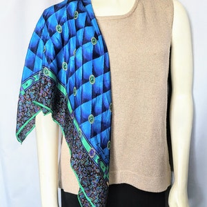 Puede incluir: Un pañuelo de seda con estampado azul y negro con un diseño geométrico y un borde de cachemira está drapeado sobre una camiseta sin mangas beige. El pañuelo tiene detalles en verde y adornos circulares.