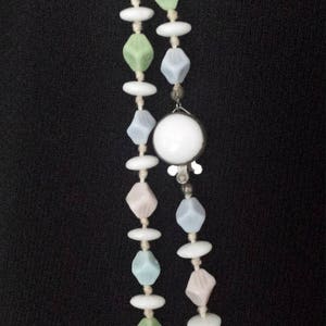 May include: A vintage necklace featuring two strands of beads in pastel colors. The beads include diamond-shaped and oval beads in shades of pink, blue, green, and white. A large white circular pendant is attached.