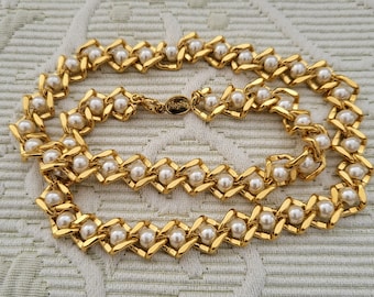 May include: A gold-toned necklace featuring a repeating pattern of faux pearls set within diamond-shaped links. The necklace has a clasp with the brand name "NAPIER" engraved. The jewelry is displayed on a textured, off-white surface.