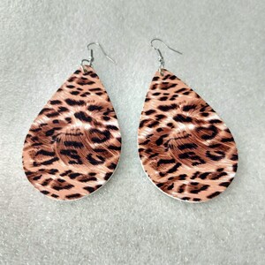 May include: A pair of teardrop earrings with a leopard print pattern. The earrings have a tan base with dark brown spots and silver-coloured ear wires. These lightweight earrings are suitable for everyday wear.