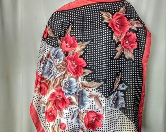 Puede incluir: Un pañuelo cuadrado con diseño floral. El pañuelo presenta un fondo negro con lunares blancos y un borde rojo. Grandes flores rojas y azules están estampadas en el pañuelo.
