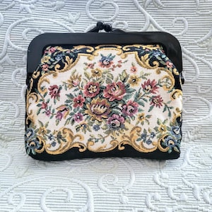 May include: A vintage tapestry coin purse with a black frame. The purse features a floral design in shades of red, pink, yellow, and blue on an off-white background, framed by black fabric.