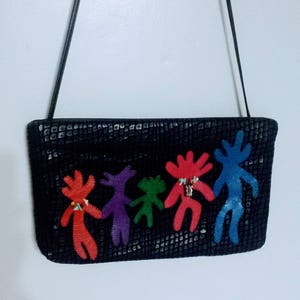 May include: Black rectangular handbag with a long strap. The bag features a textured surface and is decorated with colorful, stylized figures in red, purple, green, and blue. The figures appear to be holding hands.
