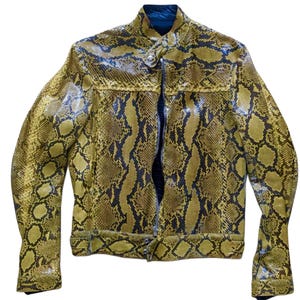 Pode incluir: Casaco com padrão de pele de cobra em tons de amarelo e preto. O casaco apresenta fecho de correr, gola alta e mangas compridas. O design imita o aspeto da pele de cobra.