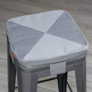 May include: A gray and white fabric chair cushion with a diamond pattern. The cushion is on a gray metal chair.