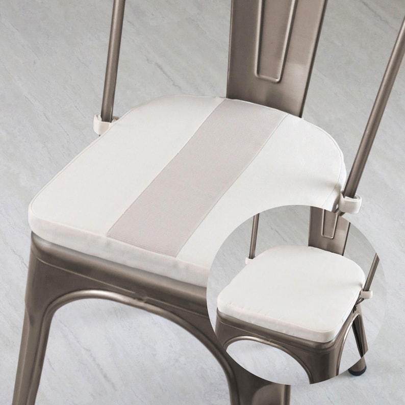 May include: A metal chair with a white cushion featuring a light gray stripe down the center. The chair has a distressed, industrial look, with a curved back and a square seat. The cushion is attached with white fasteners.