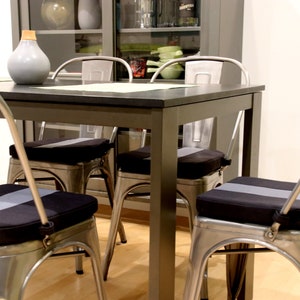 May include: A dining room set with a dark gray table and four metal chairs. Each chair has a black seat cushion with a gray stripe down the center. A gray vase sits on the table.