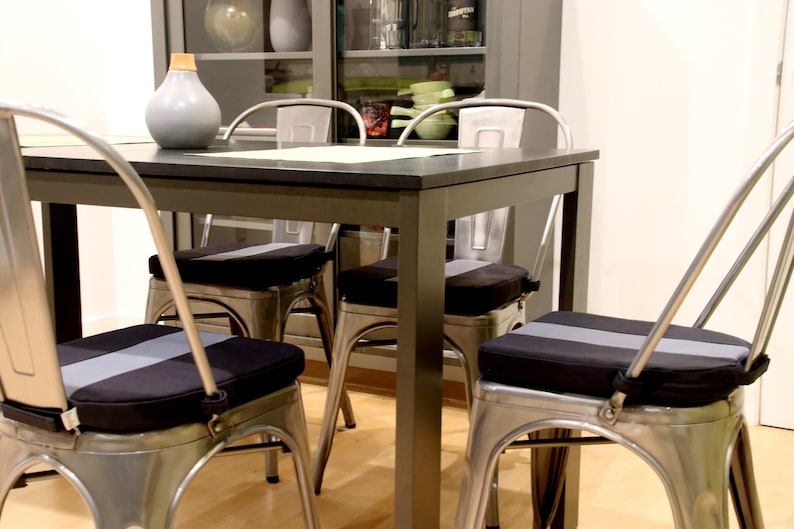 May include: A dining room set with a dark gray table and four metal chairs. Each chair has a black seat cushion with a gray stripe down the center. A gray vase sits on the table.