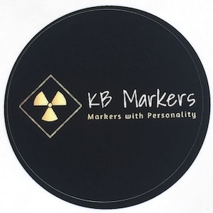 May include: A black and white sticker with a gold radiation symbol and the text "KB Markers" and "Markers with Personality".