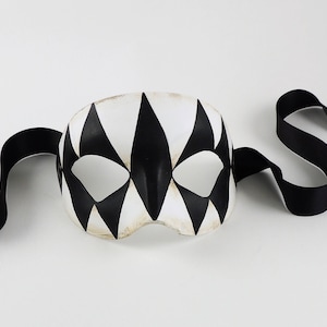 May include: A black and white masquerade mask with a geometric pattern. The mask has a black ribbon attached to it.