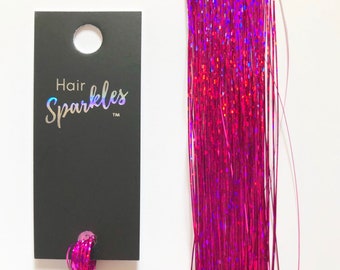 May include: A strand of pink iridescent hair tinsel with a black tag that reads "Hair Sparkles TM".