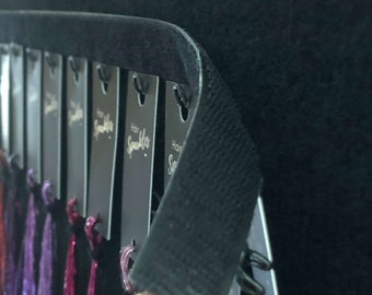 May include: A close-up of a black fabric roll with a row of black tags that say "Hair Sparkler" in white lettering. The tags are attached to strands of colorful hair extensions.