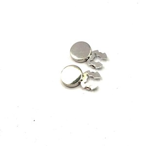 May include: Two circular silver-toned metal buttons with smooth, reflective surfaces. Each button features a distinct, jagged, multi-pronged metal attachment mechanism extending from one side, designed for secure fastening to fabric or other materials.