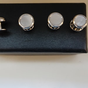 Puede incluir: Conjunto de cuatro gemelos de plata con inserciones de nácar blanco. Los gemelos son de forma ovalada y tienen un acabado pulido.