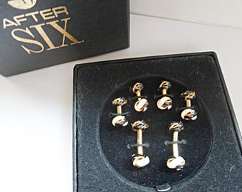 May include: A set of gold-toned cufflinks with black and white accents, presented in a black box. The box lid displays the text "AFTER SIX" in gold lettering. The cufflinks are arranged in a black velvet-lined tray.