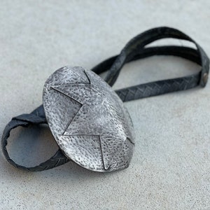 Pode incluir: Uma gravata bolo prateada com um pendente oval texturizado com um design de estrela. O pendente est&aacute; ligado a um cord&atilde;o de couro preto tran&ccedil;ado. Este acess&oacute;rio de estilo ocidental &eacute; uma joia cl&aacute;ssica.