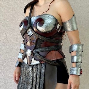 Pode incluir: Um conjunto de armadura cosplay detalhado e artesanal. A pe&ccedil;a do peito apresenta uma mistura de tons castanhos, prateados e bronze com detalhes intrincados. As prote&ccedil;&otilde;es de bra&ccedil;o e pulso a condizer completam o conjunto guerreiro. A armadura tem uma apar&ecirc;ncia met&aacute;lica texturizada.
