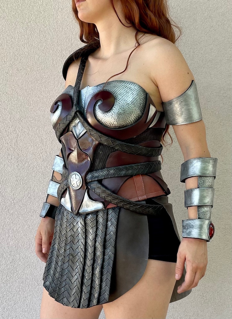 Pode incluir: Um conjunto de armadura cosplay detalhado e artesanal. A pe&ccedil;a do peito apresenta uma mistura de tons castanhos, prateados e bronze com detalhes intrincados. As prote&ccedil;&otilde;es de bra&ccedil;o e pulso a condizer completam o conjunto guerreiro. A armadura tem uma apar&ecirc;ncia met&aacute;lica texturizada.