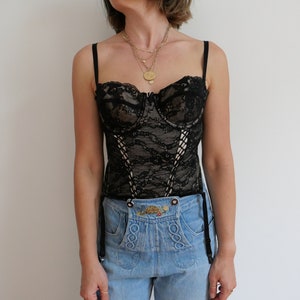 May include: A black lace corset with boning and adjustable straps. The corset is worn over a pair of light blue jeans.