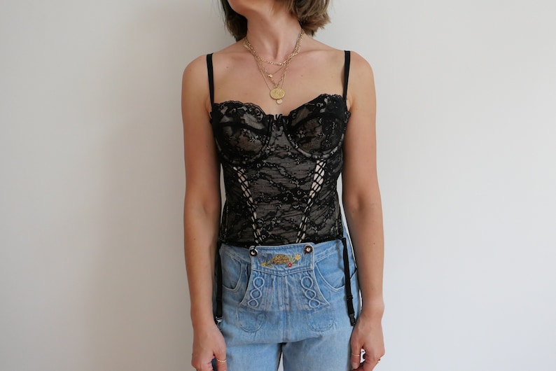 May include: A black lace corset with boning and adjustable straps. The corset is worn over a pair of light blue jeans.