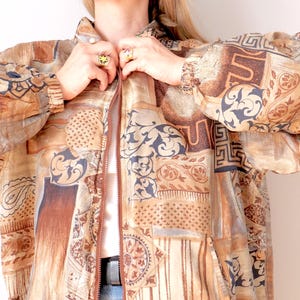 May include: A vintage patterned jacket in shades of brown, tan, and navy blue. The jacket features a repeating pattern of geometric and floral designs. It has a zipper closure and long sleeves.