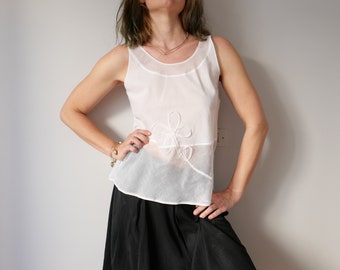 May include: White sleeveless top with a delicate floral design. The top is sheer and has a relaxed fit.