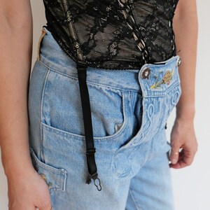 May include: A pair of light blue denim overalls with embroidered flowers and a black suspender strap. The overalls are worn with a black lace corset.