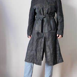 May include: A long, dark blue suede coat with a zipper closure and a matching belt. The coat has a relaxed fit and a slightly flared hem.