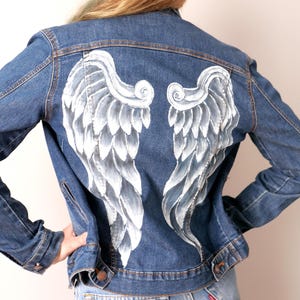 May include: A blue denim jacket with white painted angel wings on the back.