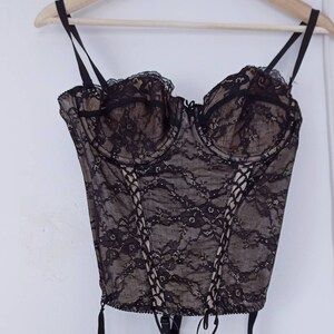 May include: Black lace corset with adjustable straps and a lace-up front. The corset has a boned structure and is designed to cinch the waist.