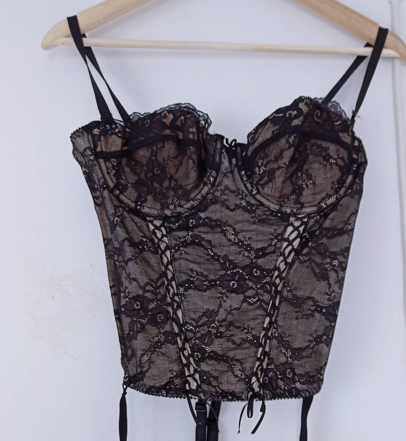 May include: Black lace corset with adjustable straps and a lace-up front. The corset has a boned structure and is designed to cinch the waist.
