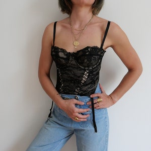 May include: A black lace corset with a sweetheart neckline and adjustable straps. The corset is worn over a pair of light blue jeans.