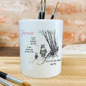 May include: White ceramic pencil holder featuring a Winnie the Pooh quote and a black and white illustration of Winnie the Pooh and Piglet walking in the woods. The holder is personalised with the name "Jasmine" and the text "Lots of love and thanks from Mia".