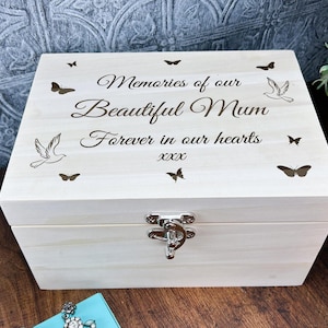 May include: A white wooden box with a hinged lid and a silver latch. The lid is engraved with the text "Memories of our Beautiful Mum Forever in our hearts xxx" and features a dove and butterfly design.