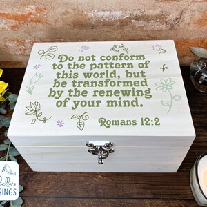 May include: A light-coloured wooden box with a hinged lid and a silver clasp. The lid is decorated with floral designs and the text "Do not conform to the pattern of this world, but be transformed by the renewing of your mind. Romans 12:2."